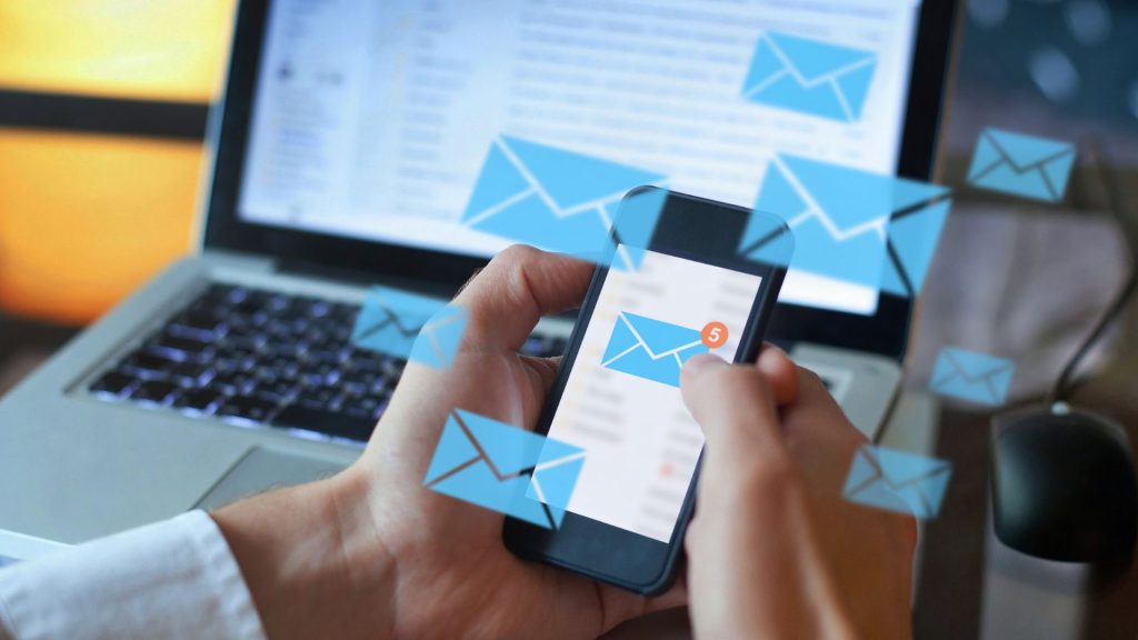 Business professional checking email on a laptop and phone.