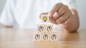 blocks stacked with peoples heads and a question marks with a light bulb at top.